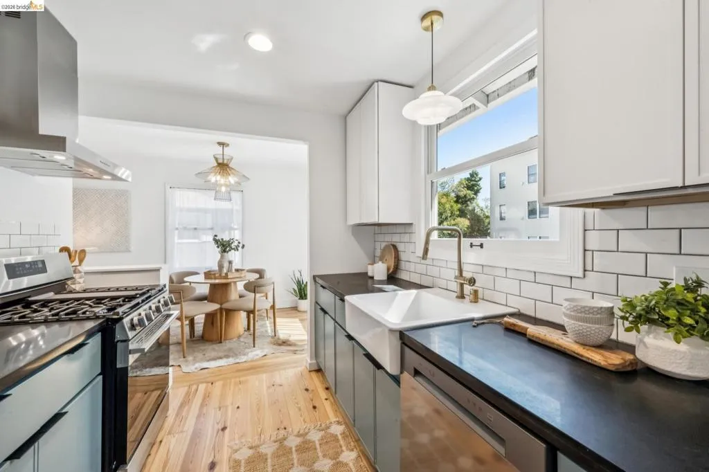 Kitchen featuring light-toned cabinetry, dark countertops, a white farmhouse-style sink, a subway tile backsplash, and wood-finish flooring