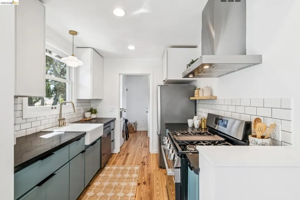Kitchen featuring wood-finish flooring, apron-front sink, white subway tile backsplash, stainless steel range hood, and two-tone cabinetry