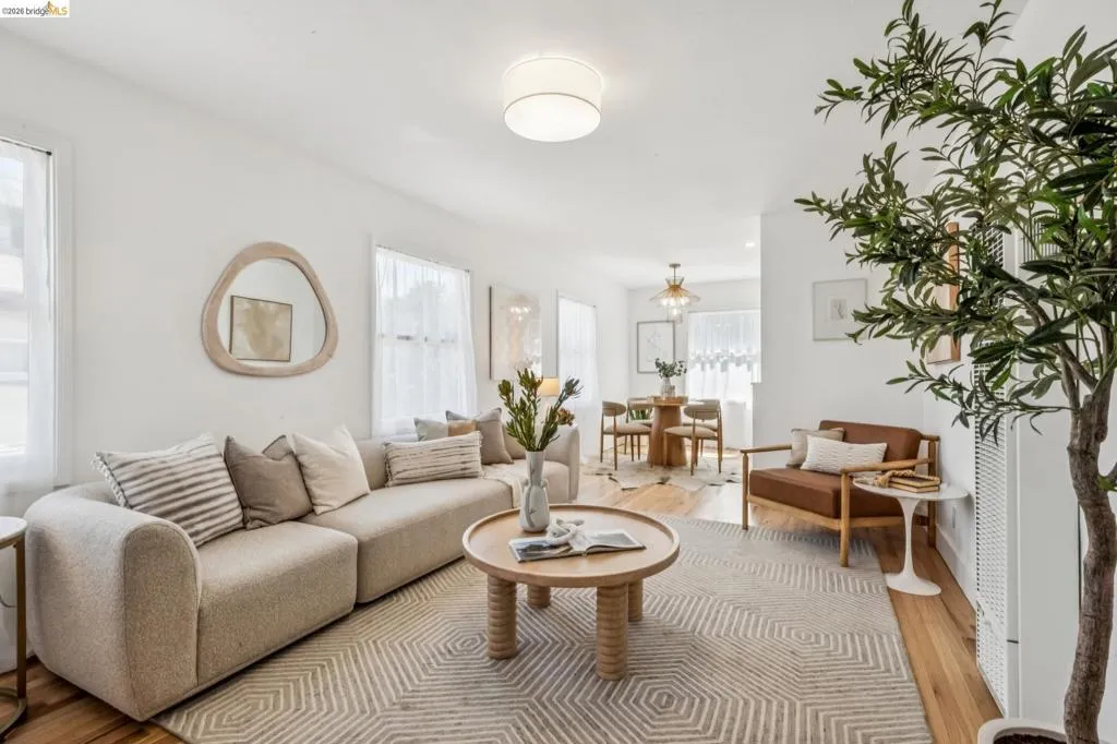 Neutral interior featuring wood-finish flooring, white walls, flush-mount drum lighting, and a multi-arm brass chandelier
