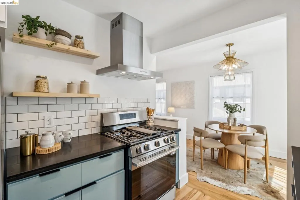 Kitchen featuring custom light-toned cabinetry, dark solid-surface countertops, white subway tile backsplash, stainless steel gas range, and a ceiling-mounted stainless steel chimney range hood