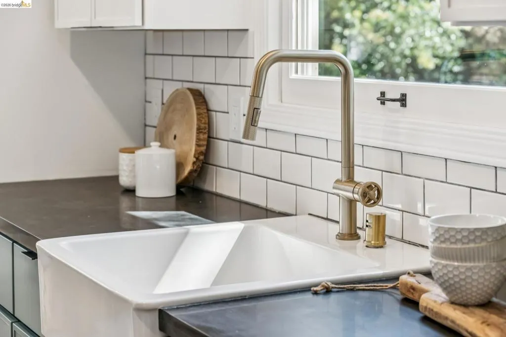 White farmhouse sink, dark solid-surface countertops, brass finish gooseneck faucet, and white subway tile backsplash