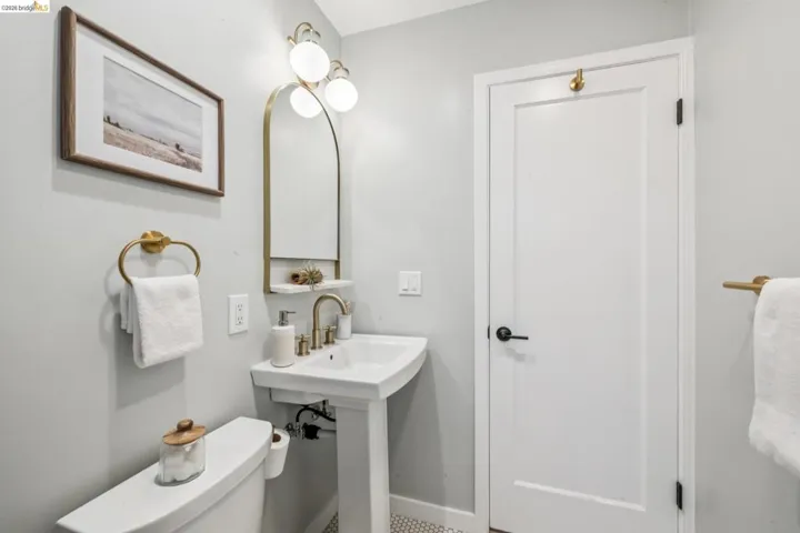 White pedestal sink with a brass faucet, arched wall mirror with integrated shelving, tri-globe brass light fixture, and brass towel hardware