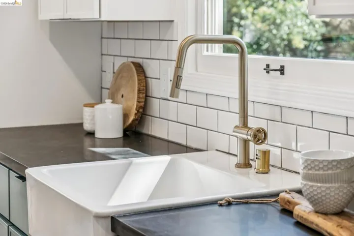 White farmhouse sink, dark solid-surface countertops, brass finish gooseneck faucet, and white subway tile backsplash
