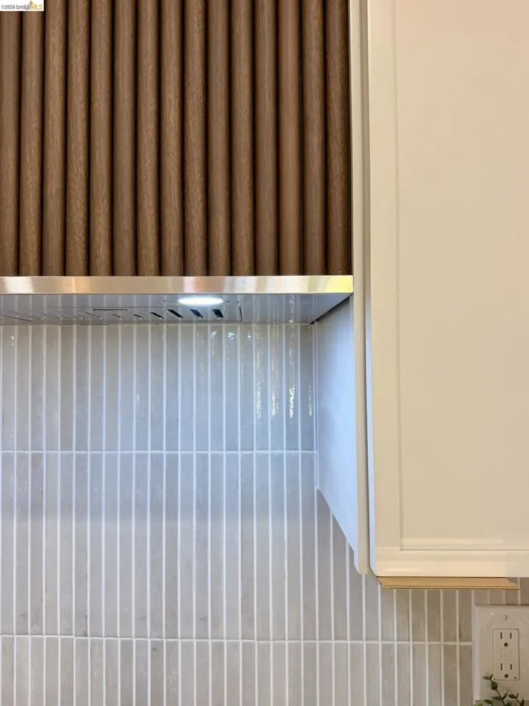 Custom range hood featuring a textured, vertical wood-finish facade, stainless steel trim, integrated lighting, and a vertical linear tile backsplash with smooth-finish cabinetry