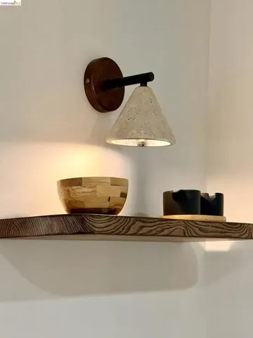 Wall-mounted sconce featuring a circular wood-finish base, matte black hardware, and a conical stone-texture shade, paired with a natural wood floating shelf