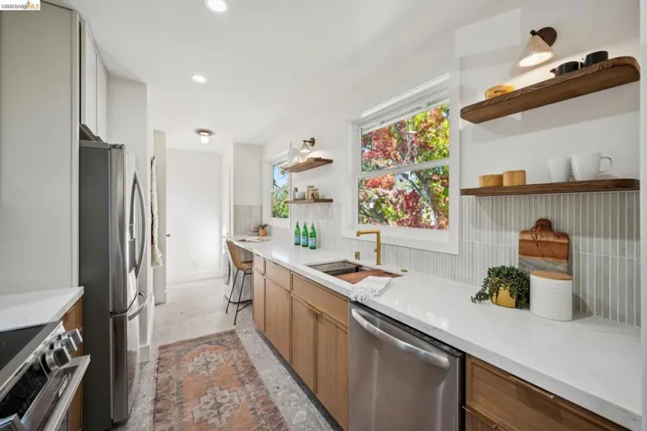 Kitchen featuring flat-panel wood cabinetry, quartz countertops, vertical tile backsplash, stainless steel appliances, and mounted wood shelving