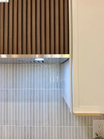 Custom range hood featuring a textured, vertical wood-finish facade, stainless steel trim, integrated lighting, and a vertical linear tile backsplash with smooth-finish cabinetry