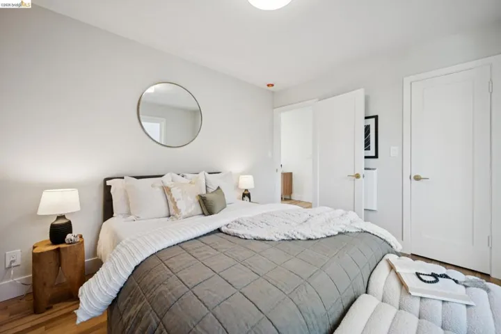Interior room featuring neutral wall paint, wood-finish flooring, a circular wall-mounted mirror, and shaker-style doors with brass-tone hardware