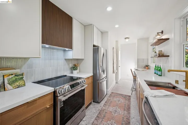 Kitchen featuring flat-panel wood and white cabinetry, stone-finish countertops, stainless steel appliances, a slatted wood range hood cover, and floating wood shelving
