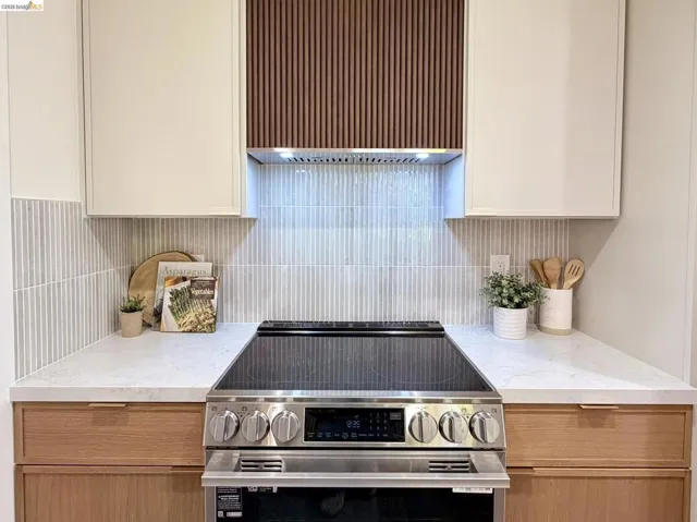 Stainless steel slide-in electric range featuring flat-panel natural wood lower cabinetry, white upper cabinetry, vertical tile backsplash, and a custom slatted wood-finish range hood