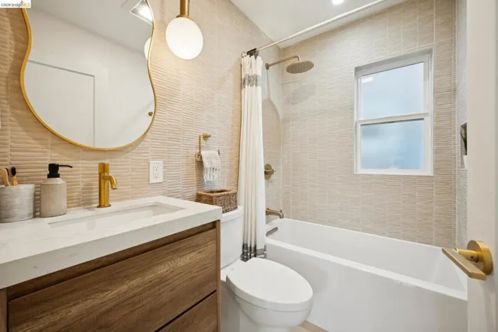 Bathroom featuring a wood-finish vanity with a stone countertop, a brass-rimmed mirror, textured wall tile, and gold-toned hardware fixtures