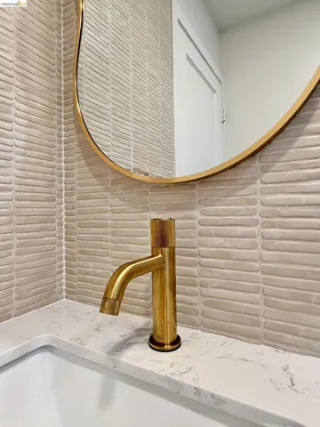 Textured elongated tile backsplash, brass-finish single-handle faucet, oval mirror with brass-tone frame, and solid-surface countertop with undermount​​‌​​​​‌​​‌‌​​‌​​​‌‌​​​‌​​‌‌​​‌‌​​‌‌​​​​ sink