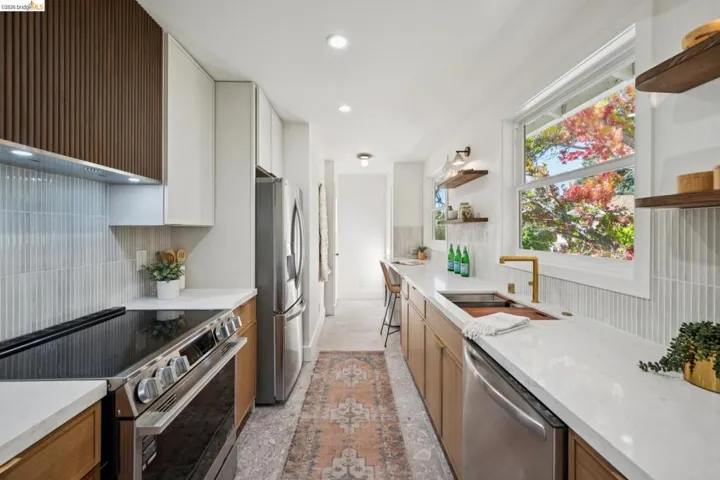 Kitchen featuring dual-toned flat-panel and slatted-wood cabinetry, quartz countertops, vertical tile backsplash, stainless steel appliances, and integrated floating wood shelving