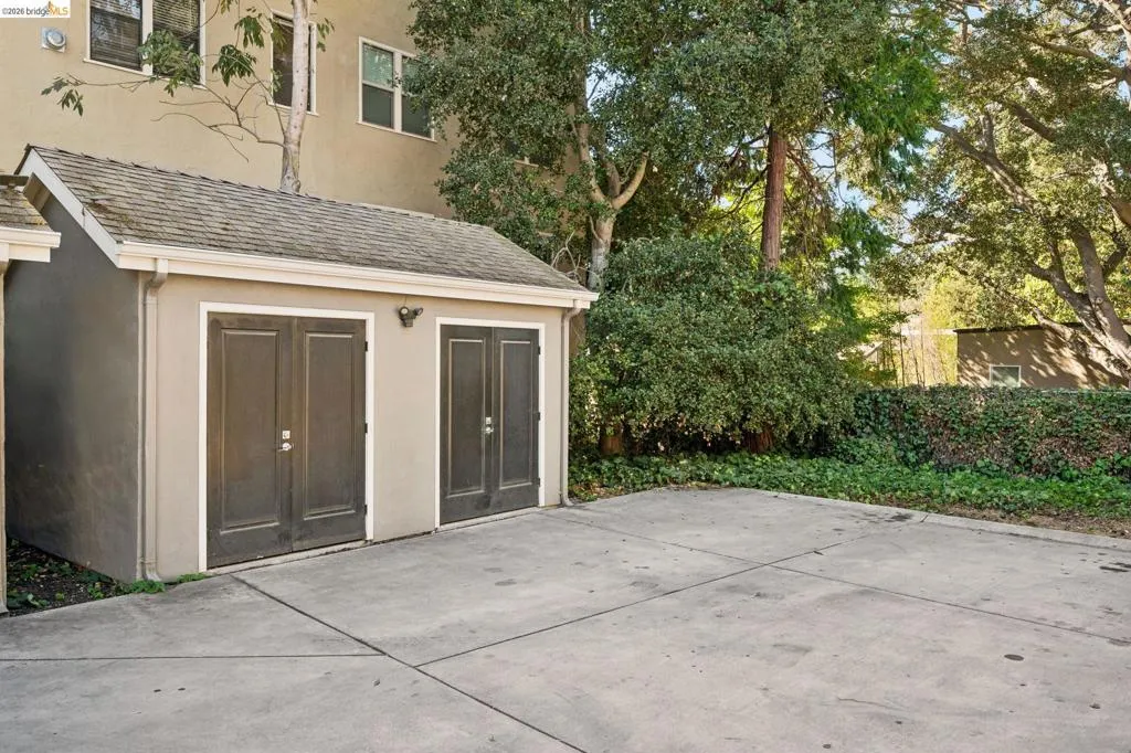 Exterior structure featuring a shingle roof, two sets of double doors, stucco siding, and an expansive concrete parking area