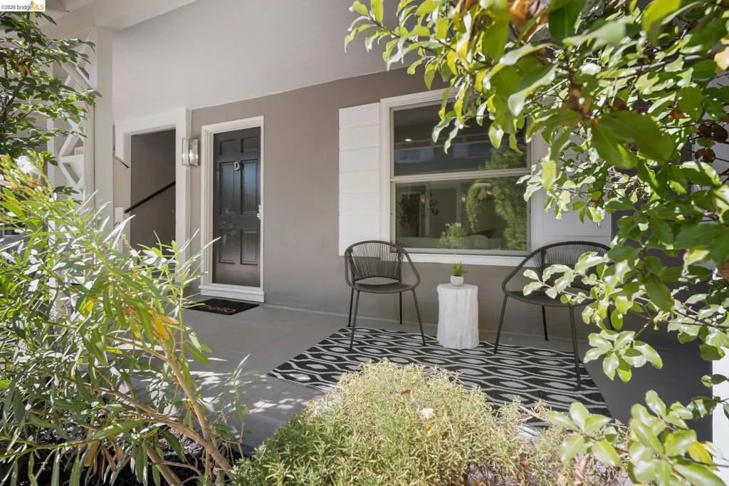 Covered porch featuring a solid-panel door with architectural hardware, neutral-toned exterior paint, white window shutters, and smooth-finish flooring