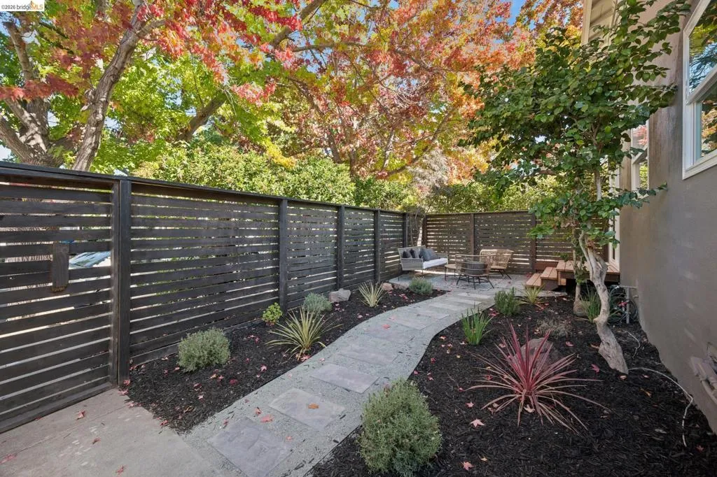 Private outdoor space featuring horizontal slat wood fencing, a stone paver pathway, dark mulch landscaping, and mature deciduous trees