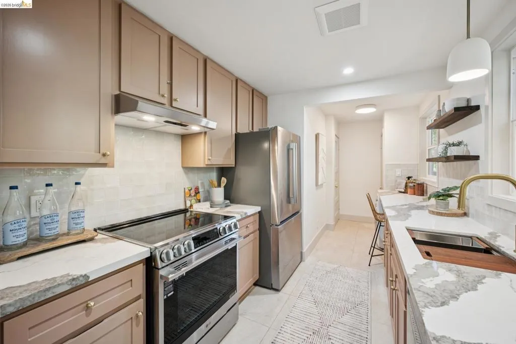 Kitchen featuring neutral cabinetry, stone-finish countertops, stainless steel appliances, ceramic tile backsplash, and floating wood shelving
