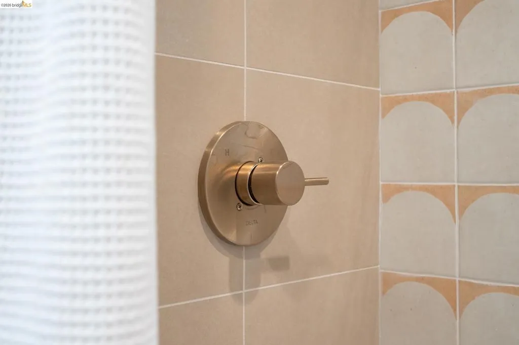 Shower enclosure featuring matte gold-finish faucet hardware, large-format square wall tile, and decorative arched-pattern accent tiling