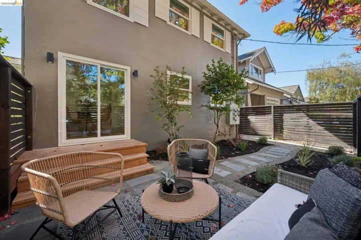 Private rear patio featuring a wood deck, stone paver pathway, horizontal slat privacy fencing, and exterior wall-mounted lighting