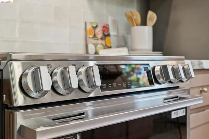 Stainless steel slide-in range with front-mounted control knobs, integrated digital display, and square-edged cabinetry, complemented by a light-toned tile backsplash