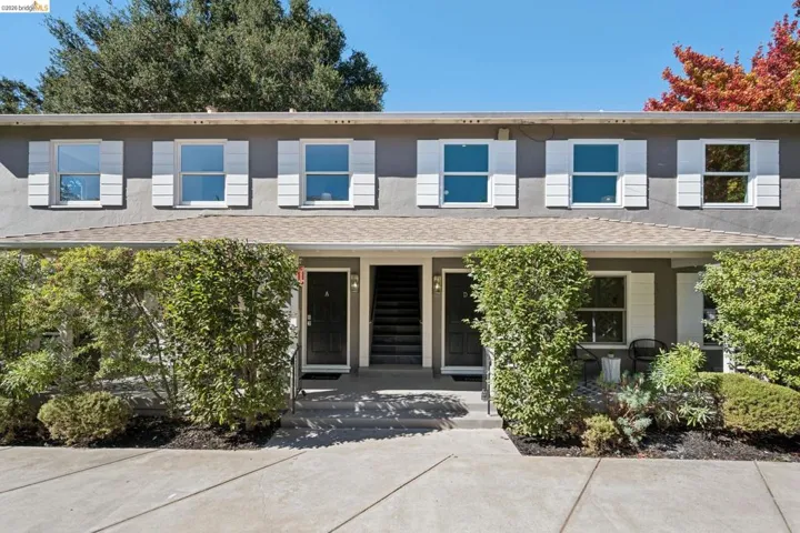 Multi-unit exterior featuring a neutral stucco facade, white shutters, double-hung windows, a concrete entryway, and mature landscaping