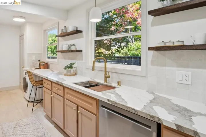 Engineered stone countertops, brass-finish faucet, shaker-style cabinetry, open wood shelving, and tiled backsplash