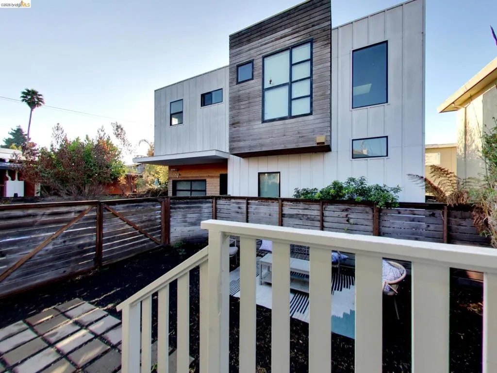 Modern architectural exterior featuring metal panel siding, horizontal wood cladding, multi-pane windows, and a private fenced yard with a paver patio Modern architectural exterior featuring metal panel siding, horizontal wood cladding, multi-pane windows, and a private fenced yard with a paver patio