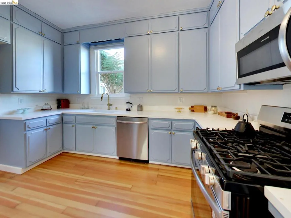 Kitchen featuring light blue cabinetry, solid surface countertops, wood-finish flooring, and stainless steel appliances including a gas range and built-in microwave Kitchen featuring light blue cabinetry, solid surface countertops, wood-finish flooring, and stainless steel appliances including a gas range and built-in microwave