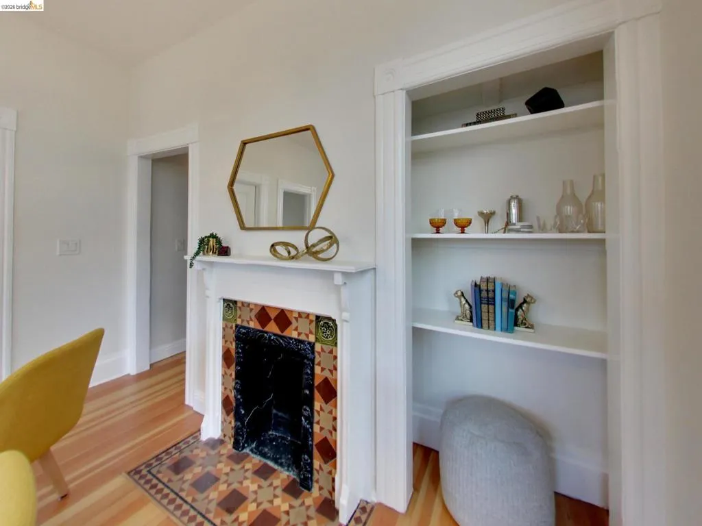 Fireplace featuring a decorative tile surround and hearth with a wooden mantel, accompanied by recessed built-in shelving and wood-finish flooring Fireplace featuring a decorative tile surround and hearth with a wooden mantel, accompanied by recessed built-in shelving and wood-finish flooring