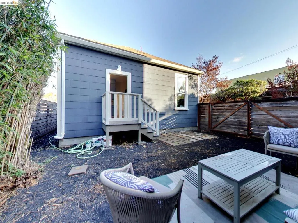Rear exterior featuring blue shingle siding, a wooden staircase, stone pavers, and perimeter wood fencing Rear exterior featuring blue shingle siding, a wooden staircase, stone pavers, and perimeter wood fencing