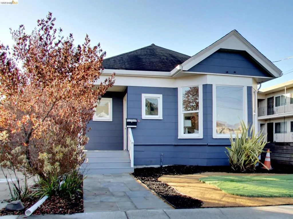 Single-story exterior featuring blue horizontal siding, a gabled roofline, a bay window, and a stone walkway Single-story exterior featuring blue horizontal siding, a gabled roofline, a bay window, and a stone walkway