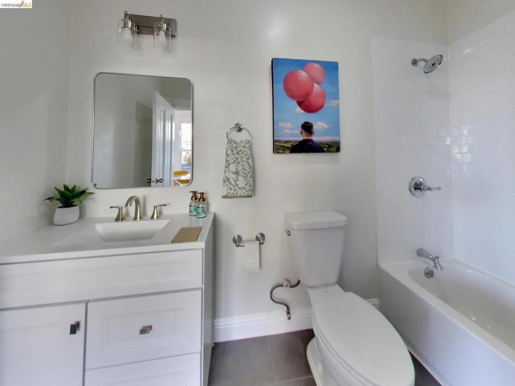 Bathroom featuring a white vanity with an integrated basin, rectangular wall-mounted mirror, brushed nickel faucet, and a tub-shower combination with white subway tile surround Bathroom featuring a white vanity with an integrated basin, rectangular wall-mounted mirror, brushed nickel faucet, and a tub-shower combination with white subway tile surround
