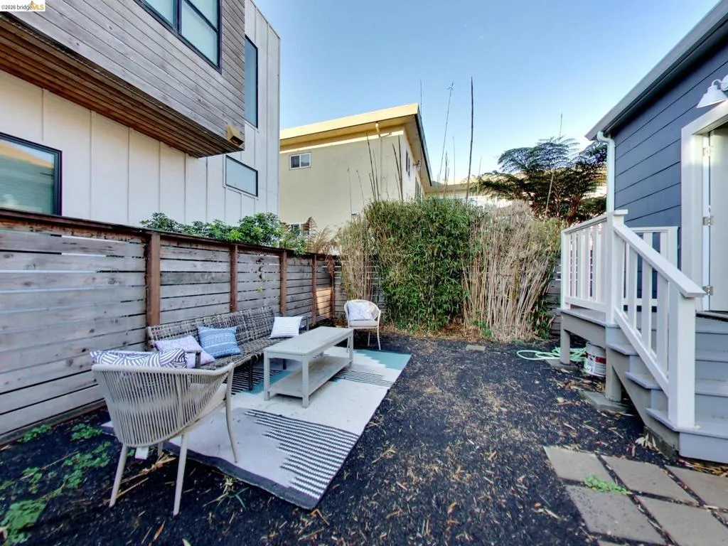 Private outdoor courtyard featuring horizontal wood privacy fencing, dark mulch ground cover, and a raised wooden staircase with white railings Private outdoor courtyard featuring horizontal wood privacy fencing, dark mulch ground cover, and a raised wooden staircase with white railings