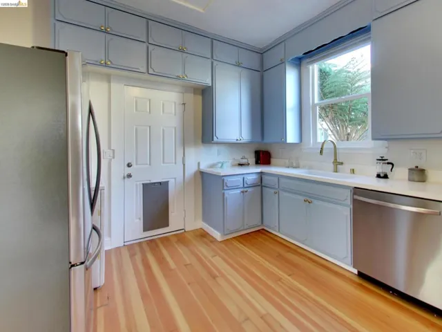 Kitchen featuring light blue custom cabinetry, white solid-surface countertops, wood-finish flooring, stainless steel appliances, and a single-basin sink with a gooseneck faucet