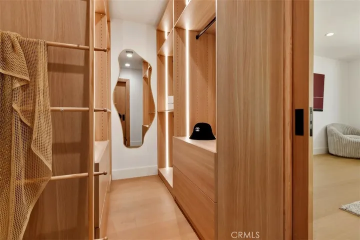  Expansive walk-in primary closet featuring custom built-in wood shelving, hanging racks, and drawers.