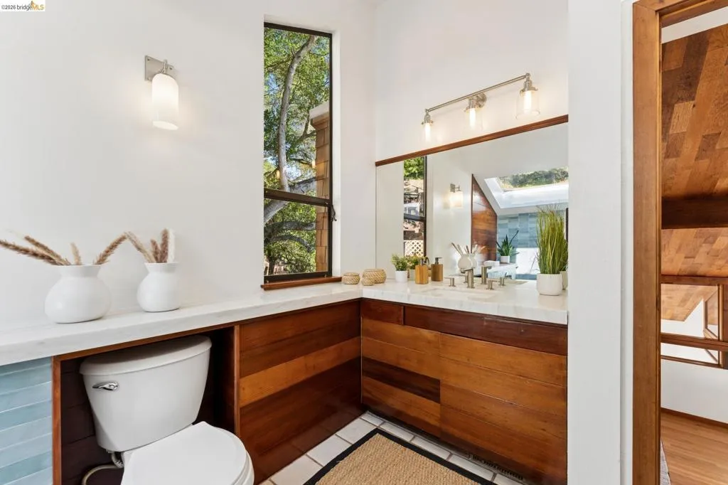 Bathroom featuring wood-paneled cabinetry and wall detailing, stone-surface vanity countertop, full-width mirror, and tall vertical window