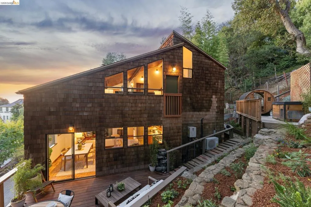 Exterior featuring dark cedar shake siding, expansive tiered wooden deck, geometric multi-pane windows, and stone-retaining wall landscaping
