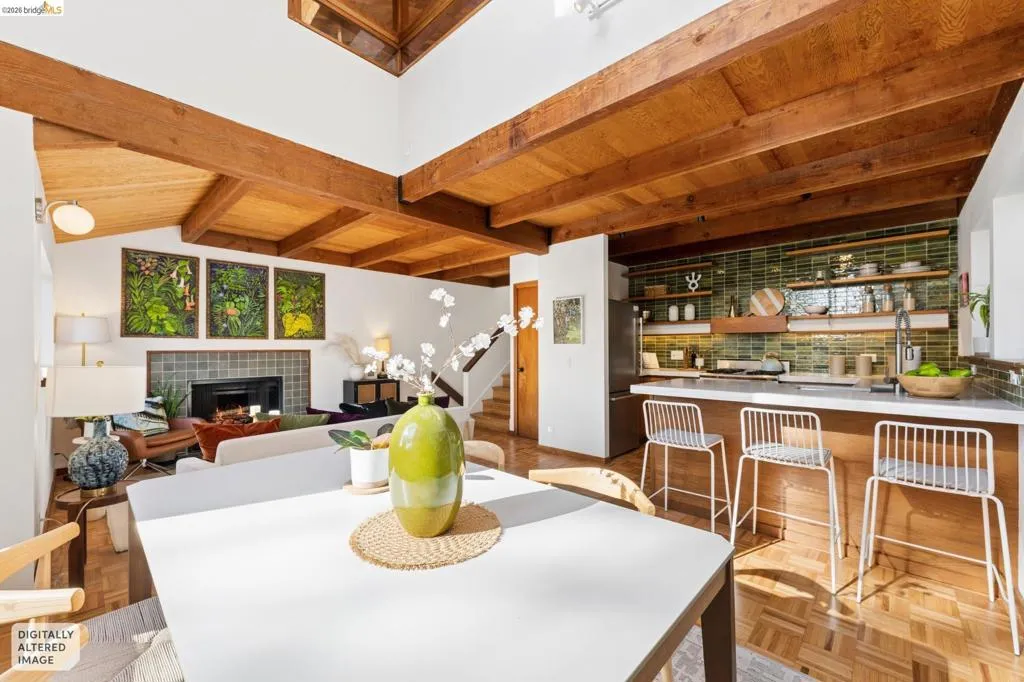 Vaulted ceilings featuring exposed wood beams, parquet flooring, a fireplace with decorative tile surround, and a kitchen equipped with a breakfast bar and green tile backsplash