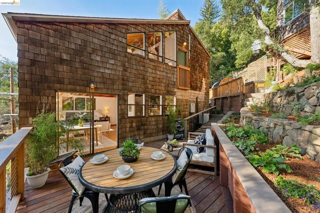 Cedar shake siding exterior featuring multi-level wooden decking, tiered stone retaining walls, and sliding glass door access