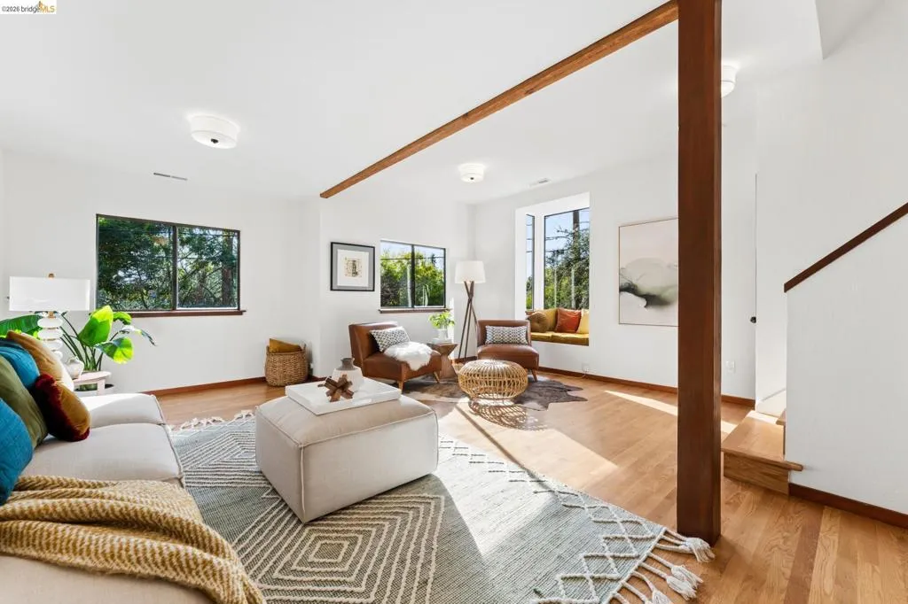 Open-concept living space featuring wood-finish flooring, exposed structural beam, recessed window seat, and neutral wall tones