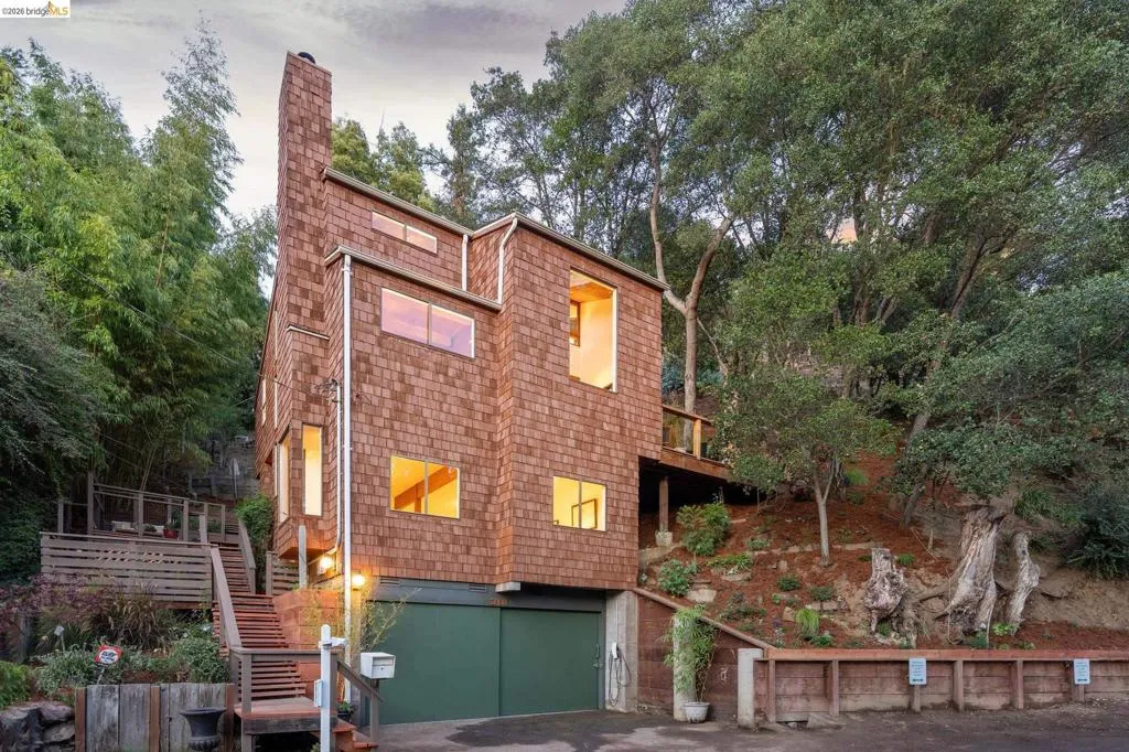 Multi-story residence featuring cedar shingle siding, a prominent chimney, an attached garage, and exterior wood staircases
