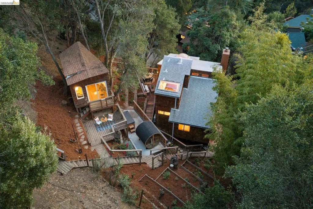 Multi-structure property featuring shingle siding, expansive wood decking, integrated skylights, a barrel-style structure, and tiered garden beds