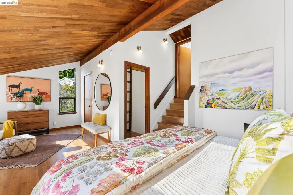 Vaulted wood-plank ceiling featuring exposed structural beams, wood-finish flooring, and wall-mounted sconce lighting