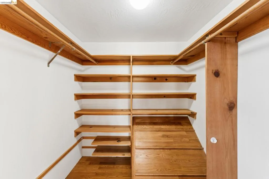 Custom storage area featuring natural wood shelving, tiered wooden platform storage, and integrated wood-finish clothing rods