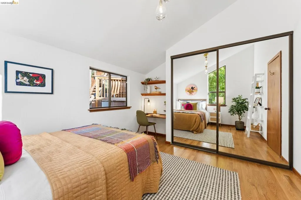 Vaulted ceilings, wood-finish flooring, built-in shelving, and floor-to-ceiling mirrored sliding closet doors