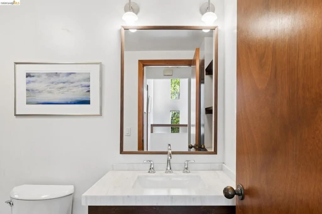 Stone-topped vanity featuring an integrated rectangular sink and polished metal widespread faucet, complemented by a wood-framed rectangular mirror and dual wall-mounted light fixtures