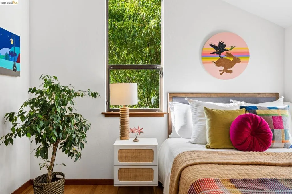 Tall vertical window with exterior greenery, wood-finish flooring, and sloped ceiling