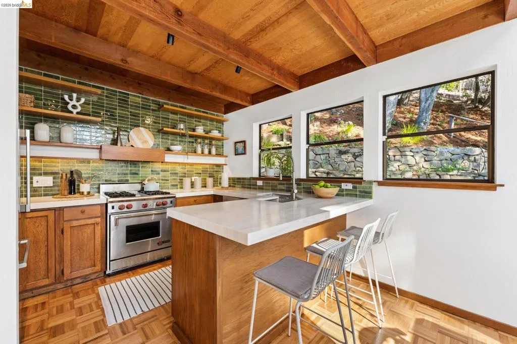 Kitchen featuring exposed wood beam ceilings, parquet wood-finish flooring, green subway-tile backsplash, stone-surface countertops, and built-in wood shelving