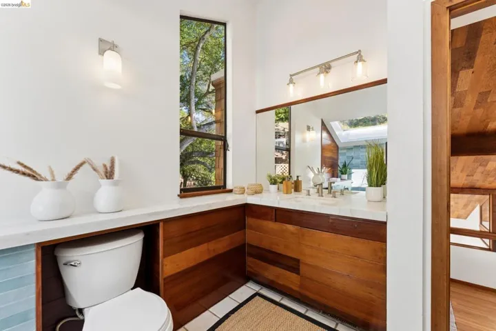 Bathroom featuring wood-paneled cabinetry and wall detailing, stone-surface vanity countertop, full-width mirror, and tall vertical window