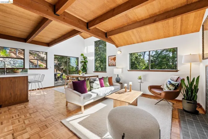 Vaulted ceilings with exposed timber beams, parquet wood-finish flooring, floor-to-ceiling windows, sliding glass doors, and a tiled fireplace surround